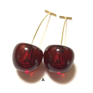 K&ouml;nnte beinhalten: Ein Paar Kirsch-Ohrringe mit goldfarbenen Stielen. Die Kirschen sind tiefrot und haben eine gl&auml;nzende Oberfl&auml;che.