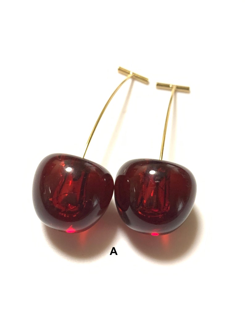 K&ouml;nnte beinhalten: Ein Paar Kirsch-Ohrringe mit goldfarbenen Stielen. Die Kirschen sind tiefrot und haben eine gl&auml;nzende Oberfl&auml;che.