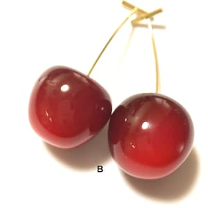 K&ouml;nnte beinhalten: Ein Paar goldene Kirsch-Ohrringe mit roten Glaskirschen. Die Kirschen sind gl&auml;nzend und haben einen leichten Farbverlauf.