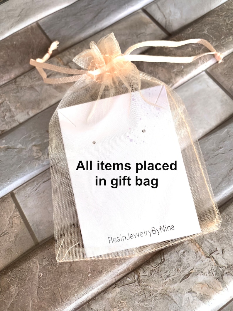Pode incluir: Uma sacola de presente transparente cor de p&ecirc;ssego com fecho de cord&atilde;o, contendo um cart&atilde;o branco. O cart&atilde;o tem o texto "All items placed in gift bag" e o nome do vendedor, "ResinJewelryByNina."