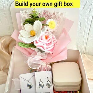 May include: A white gift box contains a crochet flower bouquet, a jewelry box, and a necklace and earrings set. The bouquet features white, pink, and yellow flowers. The text "Build your own gift box" is at the top.