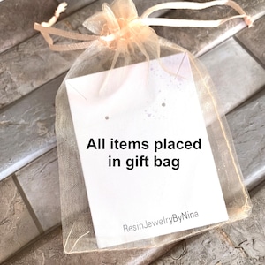 K&ouml;nnte beinhalten: Ein hellbeiger T&uuml;ll-Geschenkbeutel mit einer wei&szlig;en Karte, auf der "All items placed in gift bag" und "ResinJewelryByNina" steht.