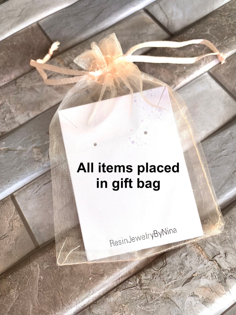 K&ouml;nnte beinhalten: Ein hellbeiger T&uuml;ll-Geschenkbeutel mit einer wei&szlig;en Karte, auf der "All items placed in gift bag" und "ResinJewelryByNina" steht.