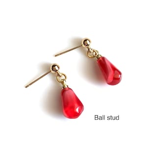 Pode incluir: Um par de brincos de bot&atilde;o dourados com contas vermelhas em forma de gota penduradas. Os brincos s&atilde;o exibidos em um fundo branco. O texto "Ball stud" &eacute; vis&iacute;vel.