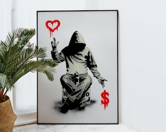 May include: A black and white stencil art print of a hooded figure holding a spray can in one hand and pointing with the other hand towards a red dollar sign. The figure is sitting on a gray box with the word "Billionaire" written on it. Above the figure is a red heart with a spray paint drip.