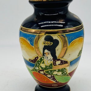 Könnte beinhalten: Eine kleine, dunkelblaue Keramikvase mit goldfarbenem Rand und aufwendigen handbemalten Details. Die Vase zeigt eine japanische Frau in traditioneller Kleidung, umgeben von goldenen und weißen Blumenmustern.