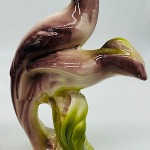 May include: A ceramic figurine of two birds perched on a green leafy branch. The birds are painted in shades of purple, brown, and white.