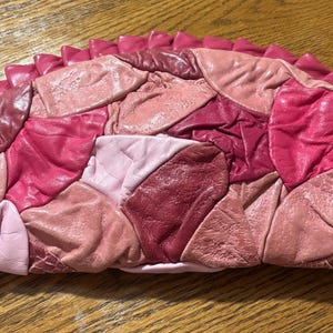 May include: A semi-circular clutch bag featuring a patchwork design of various shades of pink and red leather. The surface is composed of multiple irregular leather pieces with a ruffled, pleated border in a solid bright pink tone along the edge.