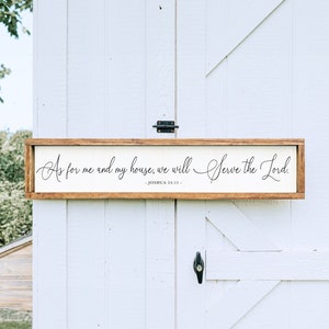 May include: A wooden sign with a white background and brown frame. The sign features a black cursive inscription that reads "As for me and my house, we will Serve the Lord. -JOSHUA 24:15-"