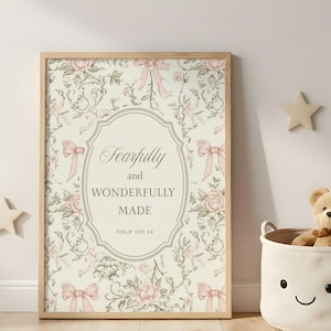 Puede incluir: Una impresión enmarcada con un diseño floral y el texto "Fearfully and Wonderfully Made" en un marco ovalado. La impresión presenta lazos y flores rosas sobre un fondo crema, con un marco de madera. Una decoración en forma de estrella está en la pared.