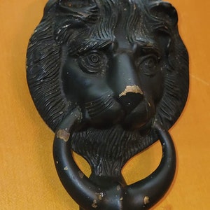 Puede incluir: Un llamador de puerta de metal negro en forma de cabeza de león con un asa de anillo.