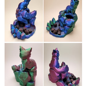 May include: A 3D printed dice tower featuring a cat perched on a rock formation. The tower is iridescent blue and green with a purple hue. The dice tower has a compartment for dice and a base with a crystal design.
