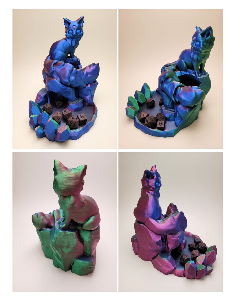 May include: A 3D printed dice tower featuring a cat perched on a rock formation. The tower is iridescent blue and green with a purple hue. The dice tower has a compartment for dice and a base with a crystal design.