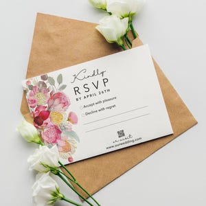 May include: A wedding RSVP card with floral detailing and the text "Kindly RSVP by April 26th" is inside a brown envelope. White flowers with green stems are arranged around the card and envelope. The website address is visible at the bottom.
