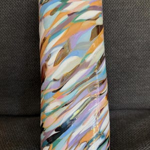 May include: A tall, cylindrical vase with a colorful, abstract design. The vase features a swirling pattern of various colors, including orange, blue, purple, and white. The glass vase is approximately 10 inches tall.