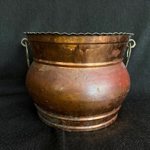 May include: A vintage copper pot with a scalloped rim and two small handles. The pot has a rounded body and a rich, aged patina, showcasing variations of brown and reddish hues. This decorative piece is suitable for home decor.