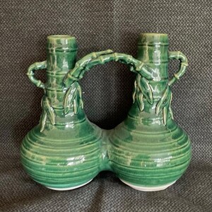 May include: A green ceramic vase with two connected bulbous sections, each with a cylindrical neck and a handle. The vase is decorated with bamboo-like details and leaves, and has a glossy finish.