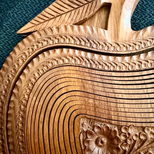 May include: A wooden apple-shaped fruit basket with intricate carved details. The basket features a leaf-shaped handle and decorative floral patterns. The natural wood color and detailed craftsmanship create a rustic, elegant look.