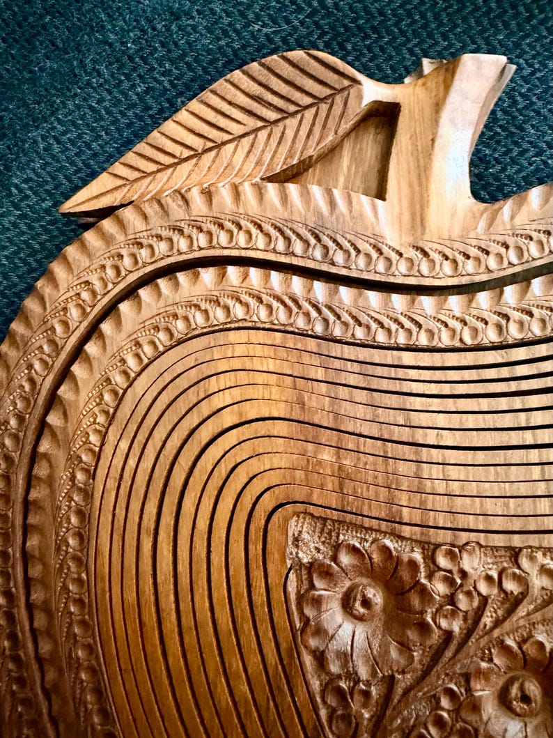 May include: A wooden apple-shaped fruit basket with intricate carved details. The basket features a leaf-shaped handle and decorative floral patterns. The natural wood color and detailed craftsmanship create a rustic, elegant look.