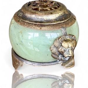 May include: A jade green, spherical incense burner with a bronze lion head detail. The lid is bronze with a decorative filigree pattern. The burner sits on a silver-colored metal base with three feet.