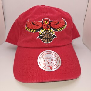 May include: Red dad hat with a team logo featuring a red bird clutching a basketball. The hat has a curved brim and an adjustable strap. A white sticker on the front reads "DAD HAT FIT UNSTRUCTURED".