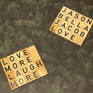 Puede incluir: Dos juegos de fichas de letras de madera que deletrean las palabras "LOVE MORE LAUGH MORE" y "JASON BELLA JACOB LOVE".