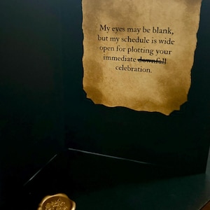 May include: A dark green greeting card featuring a parchment-style insert with the text: My eyes may be blank, but my schedule is wide open for plotting your immediate downfall celebration. A gold wax seal with a floral design is attached below.
