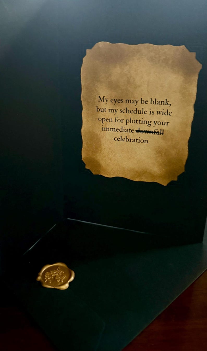 May include: A dark green greeting card featuring a parchment-style insert with the text: My eyes may be blank, but my schedule is wide open for plotting your immediate downfall celebration. A gold wax seal with a floral design is attached below.