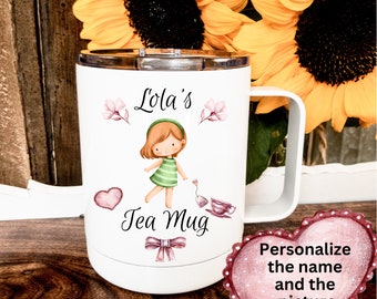 May include: White travel mug with a silver rim and handle. The mug features a cartoon girl in a green dress, the text "Lola's Tea Mug", and floral accents. A heart-shaped graphic reads "Personalize the name and the picture".