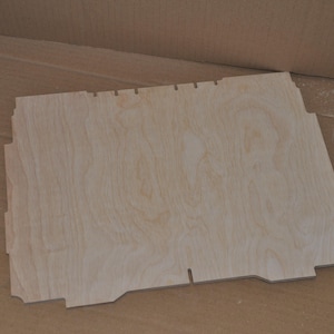 Puede incluir: Un panel de madera clara con una forma ligeramente irregular y una superficie lisa. El panel tiene un patrón de veta de madera natural.