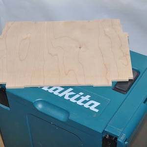 May include: A light brown wooden insert for a tool box. The insert is sitting on top of a teal blue tool box with the word "Makita" printed in white on the front.
