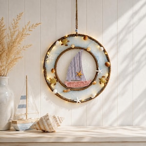 Könnte beinhalten: Ein kreisförmiger Wandbehang mit einem braunen Seilrahmen, verziert mit kleinen Meeresschildkröten, Muscheln und weißen Seesternen. Ein zentrales Segelboot-Motiv wird durch integrierte, warme LED-Lichter beleuchtet.