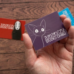 Op de afbeelding: Een paarse kaart met een witte omtrek van een kat en de tekst "スタジオジブリ STUDIO GHIBLI" in wit.