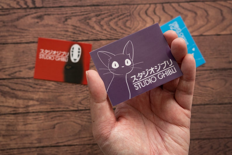 Op de afbeelding: Een paarse kaart met een witte omtrek van een kat en de tekst "スタジオジブリ STUDIO GHIBLI" in wit.