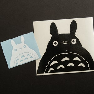 May include: Two black and white vinyl stickers of a cartoon character with large eyes and a furry body. The character is known as Totoro from the animated film My Neighbor Totoro.
