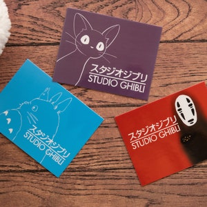 Op de afbeelding: Drie Studio Ghibli-ansichtkaarten met verschillende personages uit de animatiefilms. De eerste ansichtkaart is blauw en toont Totoro, de tweede is paars en toont de Kattenbus en de derde is rood en toont No Face.
