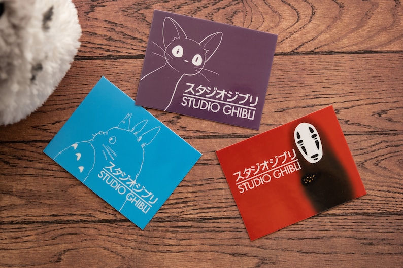 Op de afbeelding: Drie Studio Ghibli-ansichtkaarten met verschillende personages uit de animatiefilms. De eerste ansichtkaart is blauw en toont Totoro, de tweede is paars en toont de Kattenbus en de derde is rood en toont No Face.