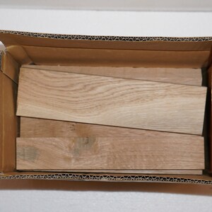 May include: A cardboard box filled with several pieces of light brown wood. The wood is stacked in a staggered pattern.