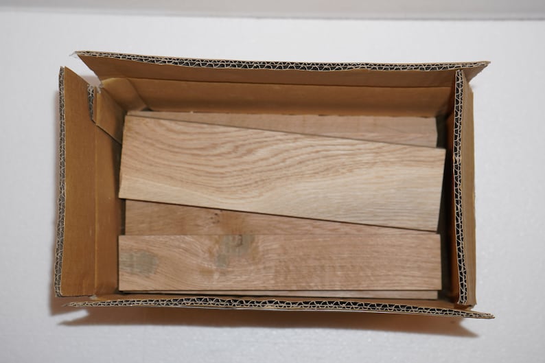 May include: A cardboard box filled with several pieces of light brown wood. The wood is stacked in a staggered pattern.