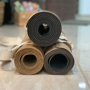 Pode incluir: Tr&ecirc;s tapetes de ioga enrolados, dois de corti&ccedil;a e um preto. Os tapetes de corti&ccedil;a s&atilde;o castanhos e t&ecirc;m uma textura natural. O tapete preto tem uma superf&iacute;cie lisa.