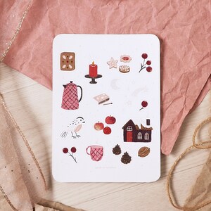 Puede incluir: Una tarjeta blanca con una variedad de ilustraciones pintadas a mano en rojo, marr&oacute;n y blanco. Las ilustraciones incluyen una tetera, un p&aacute;jaro, una casa, una vela, una estrella, una pi&ntilde;a, una taza y algunos otros objetos. La tarjeta tiene el texto "Liebe Weihnachten" en la parte inferior.