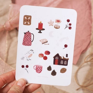 Puede incluir: Una tarjeta blanca con una variedad de ilustraciones pintadas a mano en rojo, marr&oacute;n y blanco. Las ilustraciones incluyen una tetera, un p&aacute;jaro, una casa, una vela, una estrella, una galleta de jengibre y una taza. La tarjeta tiene el texto "sarah muschalek" en la parte inferior.