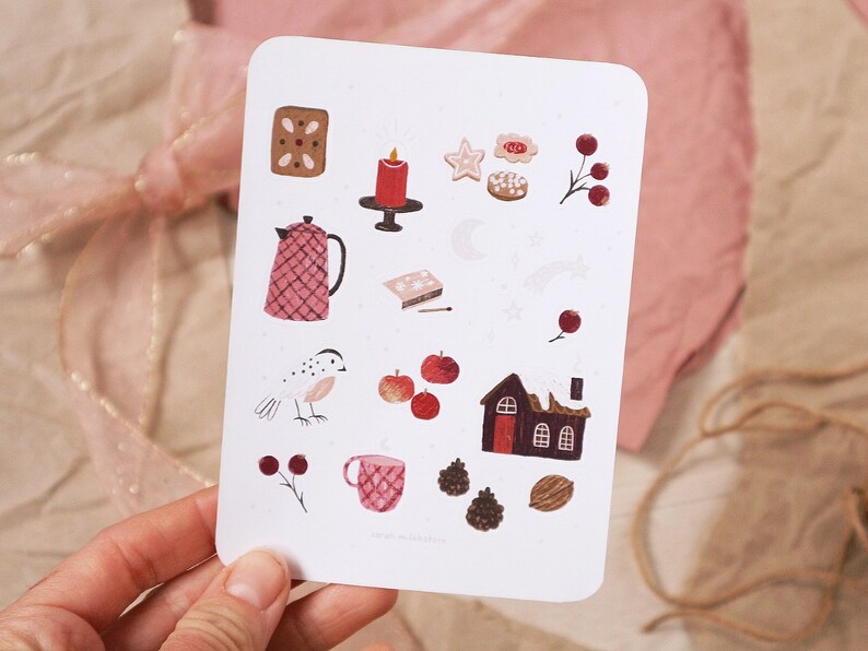 Puede incluir: Una tarjeta blanca con una variedad de ilustraciones pintadas a mano en rojo, marr&oacute;n y blanco. Las ilustraciones incluyen una tetera, un p&aacute;jaro, una casa, una vela, una estrella, una galleta de jengibre y una taza. La tarjeta tiene el texto "sarah muschalek" en la parte inferior.