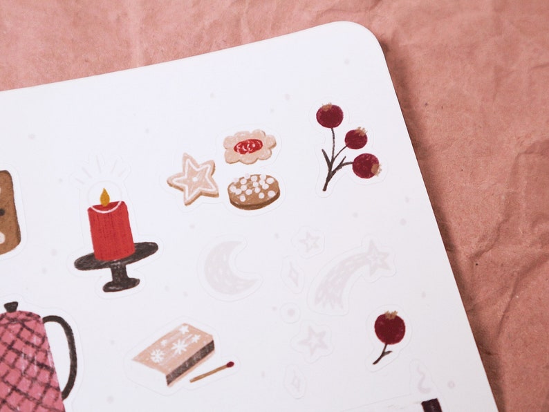 Puede incluir: Una hoja de pegatinas con una variedad de ilustraciones de tem&aacute;tica invernal, que incluyen una vela, galletas de jengibre, estrellas, una luna y bayas de acebo.
