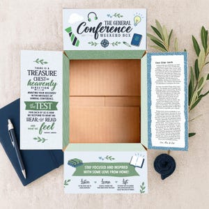 May include: An open cardboard box with printed text and graphics. The box is labeled "The General Conference Weekend Box." Text includes "Treasure Chest of Heavenly Direction" and "Stay Focused and Inspired." A navy blue pen and notebook are visible.