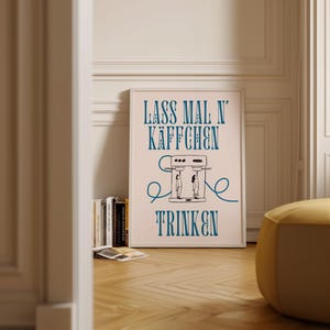 Peut inclure: Une affiche encadrée rose avec une illustration bleue et noire d'une cafetière et le texte "Lass mal n' Käffchen trinken".
