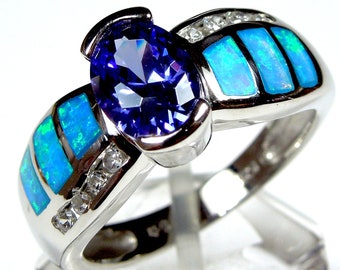 Può includere: Un anello d'argento con una grande pietra preziosa ovale di colore viola circondata da pietre preziose più piccole e trasparenti. La fascia dell'anello è decorata con intarsi di opale blu e verde.