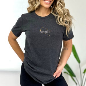 May include: A dark gray t-shirt with a gold constellation design and the word "gemini" printed on the front.