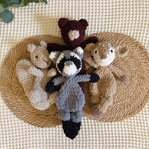 May include: A collection of four handmade crochet plush toys featuring a dark brown bear, a light beige squirrel, a grey and black raccoon, and a tan deer. Each stuffed animal is crafted from soft, textured yarn with embroidered facial details.