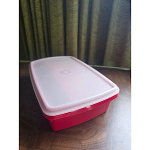 May include: A rectangular food storage container with a solid red base and a translucent, semi-opaque white lid. The container features rounded corners and a smooth, flat surface on the top of the lid, designed for secure food preservation.